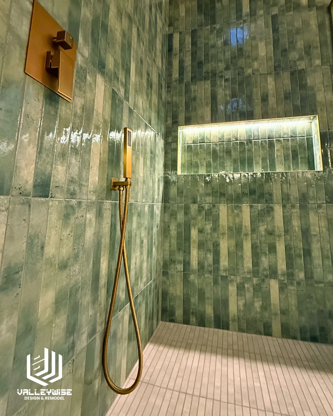 Green tiled shower with a lit niche and gold handheld shower fixture